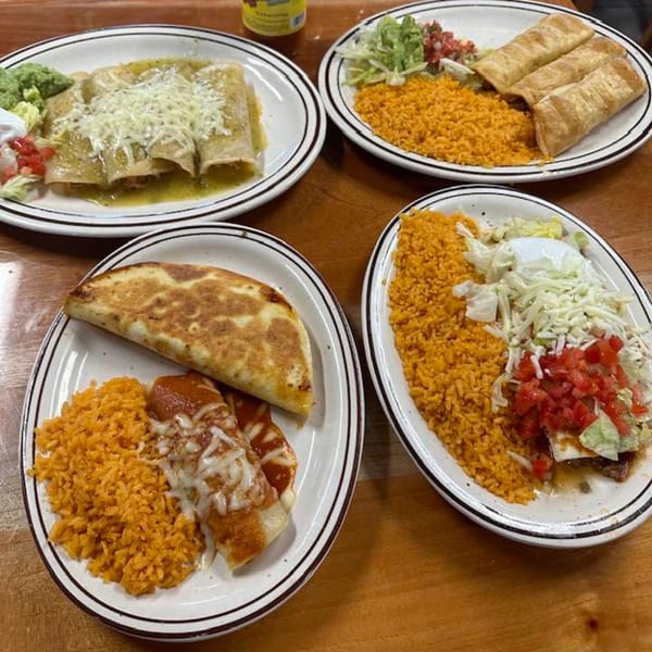 Four plates of Mexican food, including enchiladas, flautas, quesadilla, and rice, on a wooden table.