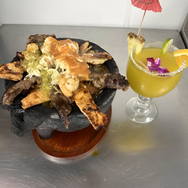 A molcajete filled with grilled meats, shrimp, and green sauce, next to a garnished margarita.