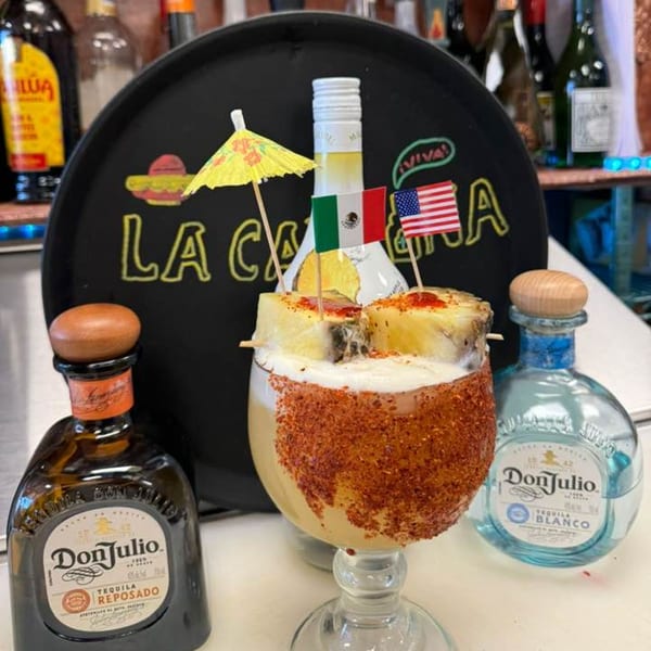 A La Cantina Mexican margarita with pineapple, chili rim, and flags, flanked by Don Julio tequila bottles.